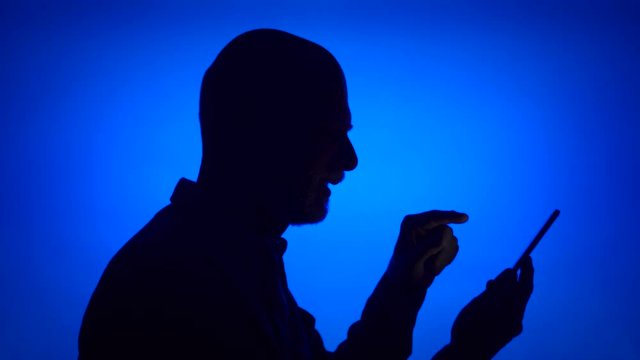 Silhouette of senior man using mobile on blue background. Male's black contur of face in profile receiving good news on cellphone excited. Concept of success and being winner