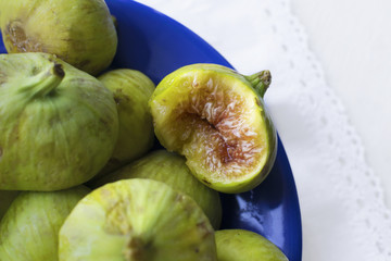 Green figs fruits on blue dish, bitten fruit, flat lay, close-up