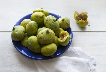 Green figs fruits on blue dish, bitten fruit
