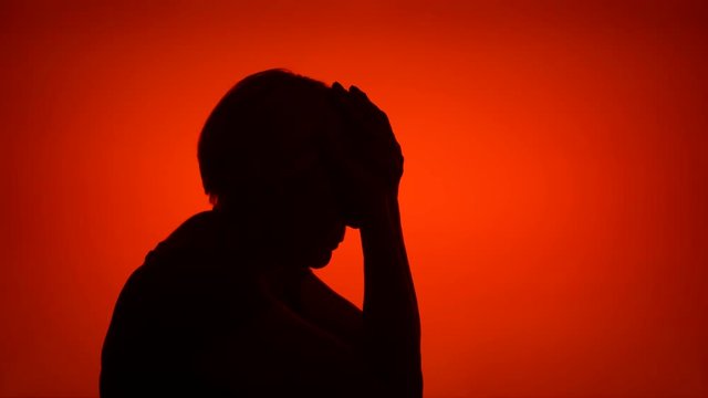 Silhouette of senior frustrated woman. Female's face in profile in despair on red background. Black contour shadow of sad grandmother's half-face showing strong negative emotions