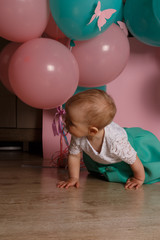 Obraz premium a little girl is sitting on the floor, on a pink background, near the balloons, with a pacifier. celebration. birthday, one year old. Little Girl with soother.