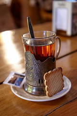 Glass of tea in an old vintage metal holder with cookie and sugar on a wooden table