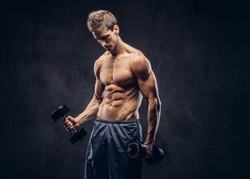 Handsome shirtless man with stylish hair and muscular ectomorph body doing the exercises with dumbbells.