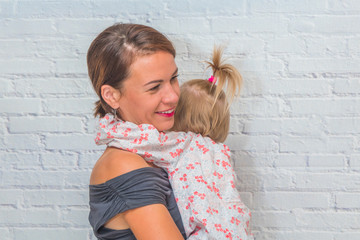a mother and daughter in her arms against a white brick wall