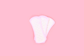 Daily sanitary pads on a pink pastel background with rose petals. The concept of ease, security, femininity.
