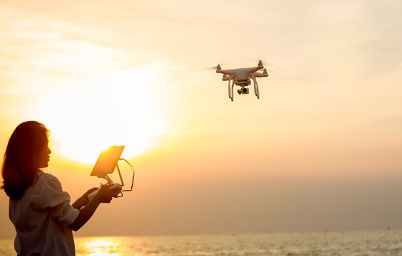 Silhouette of young woman using drone at sunset for photos and video making - Happy woman having fun with new technology trends in sky and sea.