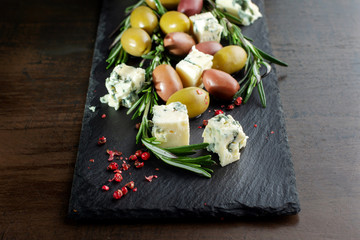 Cheese dor-blu, olives and basil are lined on a black slate.