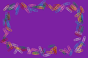 colored paper clips lying in a frame shape on a purple background. free space for advertising text. concept of office chancery