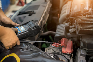 Mechanic use voltmeter checking voltage of car battery in car service centre.