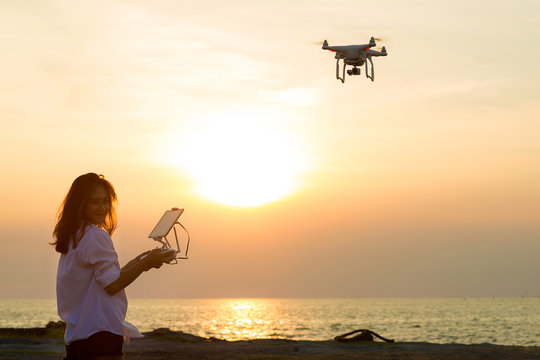 Silhouette of young woman using drone at sunset for photos and video making - Happy woman having fun with new technology trends in sky and sea.