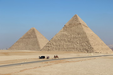 Fototapeta na wymiar Zwei Pyramiden, darunter Cheops, in Ägypten bei Kairo mit einer Straße und ein Auto und Kamele davor.