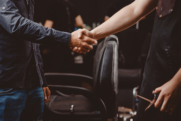 Obraz premium Witamy w sklepie fryzjerskim. Klient mężczyzna i uścisk dłoni fryzjera, w tle salon fryzjerski miejsce pracy włosów.