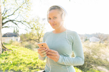 Junge Sportlerin steht im Park und hört Musik vom Smartphone
