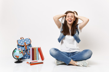 Portrait of young casual joyful laughing woman student keeping hands on head sitting near globe...