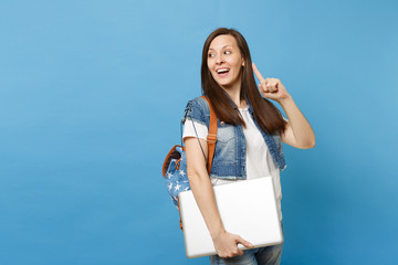 Young excited cute woman student with backpack having new idea pointing index finger up holding laptop pc computer isolated on blue background. Education in university. Copy space for advertisement.