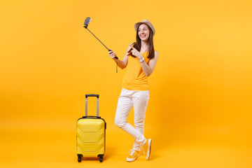 Happy tourist woman in summer casual clothes, hat doing selfie shot on mobile phone isolated on yellow orange background. Passenger traveling abroad to travel on weekends getaway. Air flight concept.