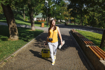 Traveler tourist woman in yellow summer casual clothes and hat with suitcase, city map walking in city outdoor. Girl traveling abroad to travel on weekends getaway. Tourism journey lifestyle concept.