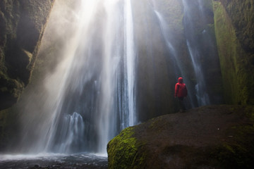 Hombre con abrigo rojo en la cascada oculta Gljufrafossl en Islandia