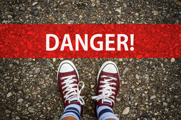 man legs in sneakers standing next to red line and word DANGER