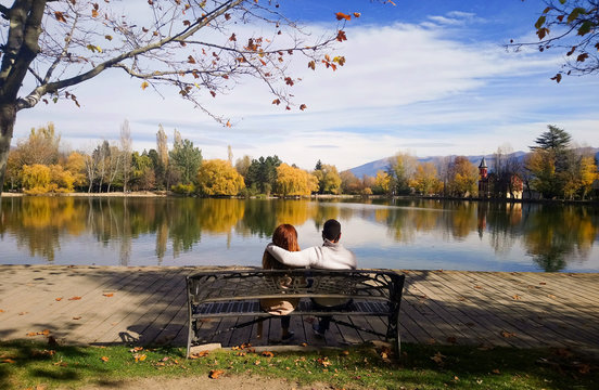 Autumn love, young loving couple sitting on a bench in front of the lake of Puigcerda, Spain