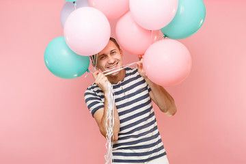 Portrait of fascinating young happy man wearing striped t-shirt holding colorful air balloons...