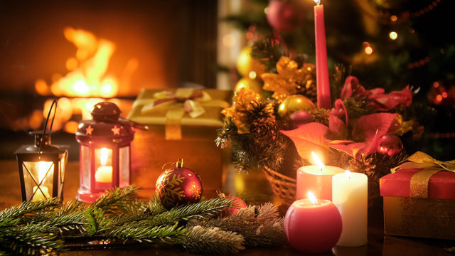 Closeup toned image of Christmas decorations on wooden table against burning fireplace