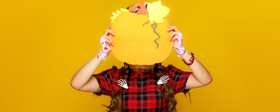 woman on yellow background holding pumpkin in front of face