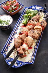 Traditional Greek souvlaki barbecue skewer with tomato onion salad and  tzatziki as closeup on a plate