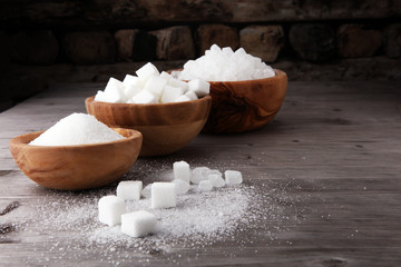 Bowl with white sand, crystal and lump sugar on wooden background.