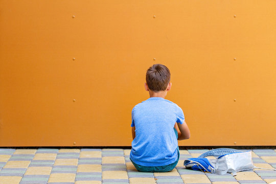 Sad alone boy sitting near colorful wall outdoors