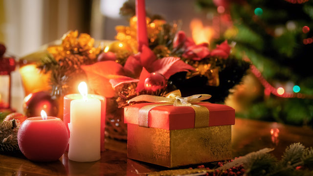 Closeup image of burning candles standing against gift box and Christmas tree