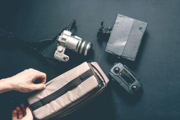 overhead top view of hand put camera accessories in bag on dark background