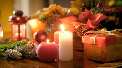 Closeup image of burning candles on wooden table against Christmas wreath