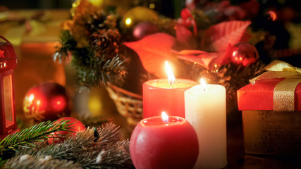 Closeup image of three burning candles and beautiful Christmas wreath on wooden table