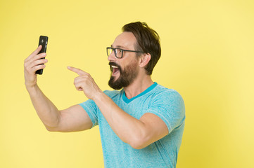 Guy eyeglasses cheerful pointing at smartphone. Man happy user interact application for smartphone. Guy bearded interact mobile interface application. Man excited about new opportunities