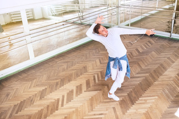 Modern art dancer dressed in white clothes listening a music with smartphone using a headphones and dancing in mirror hall