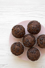 Chocolate cupcakes on pink plate on white wooden background, top view. Flat lay, overhead, from above. Close-up.