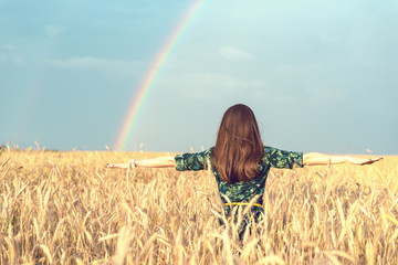Freedom. Happy smiling woman with open hands in wheat field with Golden spikelets looking up at the sky on rainbow background