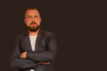 man with a beard crossed his hands looking into the distance on a dark background, emotions seriousness, making plans