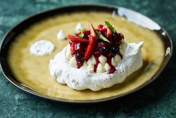 Pavlova meringue cake with fresh berries and custard cream on plate on green marble table background, close-up 
