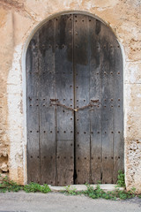 Fototapeta na wymiar Rustic brown vaulted old wooden door on stone building