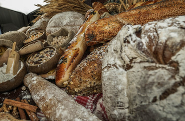 Bread background. Brown and white whole grain loaves wrapped in kraft paper composition on rustic dark wood with wheat ears scattered around. Baking and home bread making concept. Soft toning
