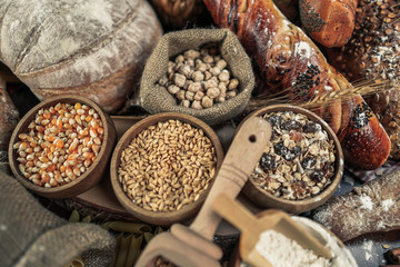 Bread background. Brown and white whole grain loaves wrapped in kraft paper composition on rustic dark wood with wheat ears scattered around. Baking and home bread making concept. Soft toning
