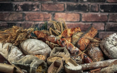 Bread background. Brown and white whole grain loaves wrapped in kraft paper composition on rustic dark wood with wheat ears scattered around. Baking and home bread making concept. Soft toning
