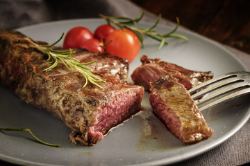 Grilled rump steak with rosemary garnish and tomatoes on a gray plate, rustic style