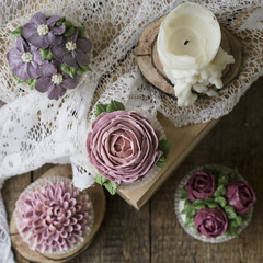 Cupcakes decorated with cream flowers: roses, peonies, chrysanthemums, poppies, scabiosa, on a wooden background with a lacy napkin. Close up