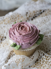Obraz na płótnie Canvas Cupcake decorated with cream rose on a wooden background with a lacy napkin. Close up
