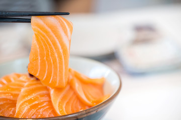 Close up salmon slice took by chopsticks. salmon topped by fresh salmon served with wasabi and soy sauce, donburi rice. image for background, copy space, decorate and menu list.