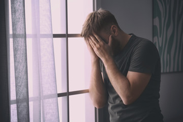 Fototapeta na wymiar Depressed young man near window at home
