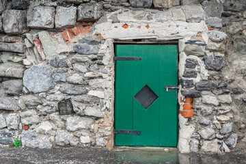 Small green wooden door locked with a padlock on a grey old stone wall